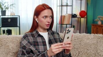 ung kvinna på Hem inlärning ny språk använder sig av mobil app och upprepa ord högt med fokus och glädje. caucasian rödhårig flicka på soffa njuter pedagogisk bearbeta praktiserande uttal och Tal video