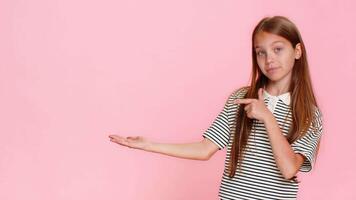 ung barn flicka lyckligt poäng till tom område på färgrik bakgrund, inbjudande tittare till se på imaginär annons, text eller logotyp med glad uttryck öppen gest. skola unge isolerat på rosa bakgrund video