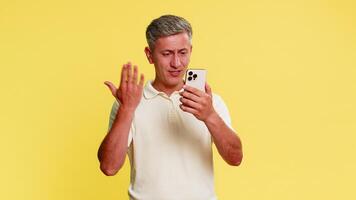 di mezza età uomo rabbiosamente urla in smartphone durante Telefono chiamata, agitando mani mostrando frustrazione e irritazione, urgente fine pulsante. tipo esprimendo discussione emozione isolato su giallo sfondo video