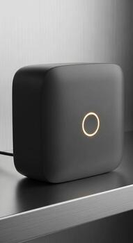 Sleek modern dark gray smart home device with a subtle illuminated circular emblem on a reflective surface photo