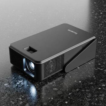 Compact black portable projector with built in stand resting on a speckled dark surface photo