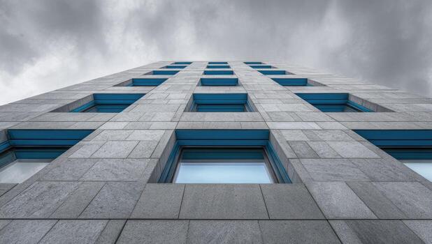 Low-angle view of a modern, light gray building facade with numerous square windows framed in teal blue photo