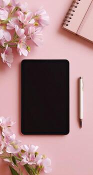 Flat lay of a tablet, pink flowers, notebook, and pen on a pink surface photo