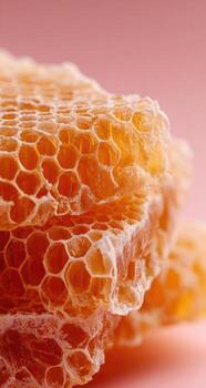 Close-up of honeycomb pieces, light orange color, stacked against a soft pink background photo