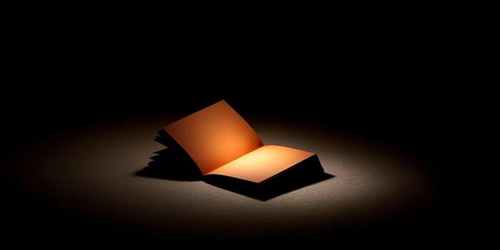 An open blank notebook is illuminated by a warm spotlight on a dark textured surface creating a dramatic and mysterious atmosphere photo