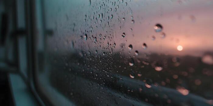 Raindrops cling to a window pane with a blurred sunset sky in the background creating a serene atmospheric scene photo