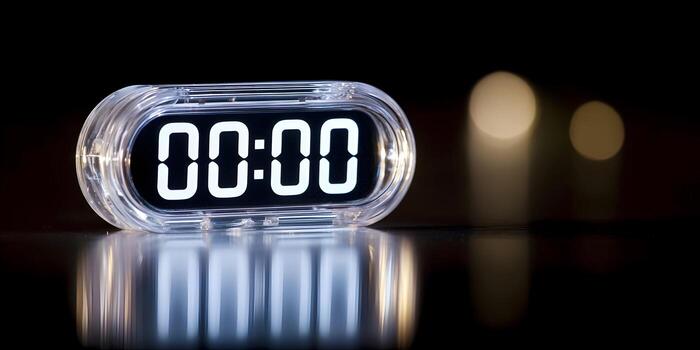 A transparent digital timer displaying 0000 sits on a reflective dark surface with out of focus lights photo