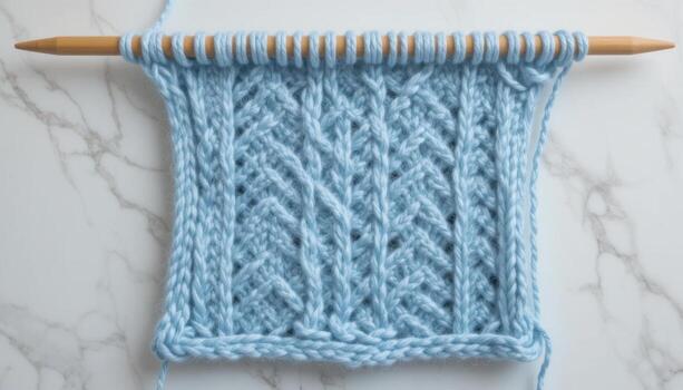 Knitting in Progress With a Light Blue Pattern on a Wooden Needle on a Marble Surface photo