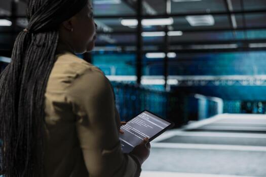 Data center admin uses tablet to monitor hardware for potential failures, improving system stability. Server hub IT professional configures supercomputers settings with device to increase uptime photo