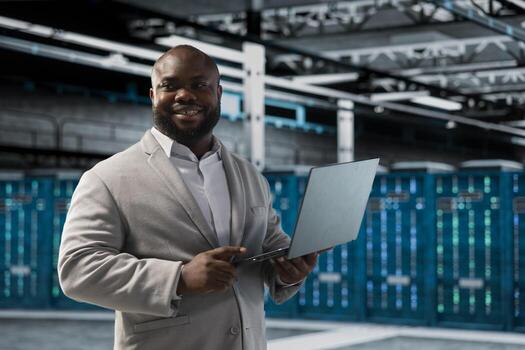 Happy data center engineer using laptop to automate errors detection, debugging software issues. Cheerful server hub IT expert looking for network issues affecting rigs, improving system stability photo