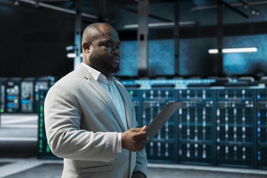 Programmer in data center updating systems using tablet, debugging app performance issues. Server hub IT expert using device, looking for malfunctions, increasing maximum efficiency and uptime photo