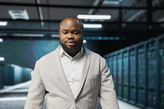 Admin walking in high tech data center, doing checkup to prolong hardware life span and avoid downtime. African american server hub IT specialist monitoring server infrastructure rigs photo