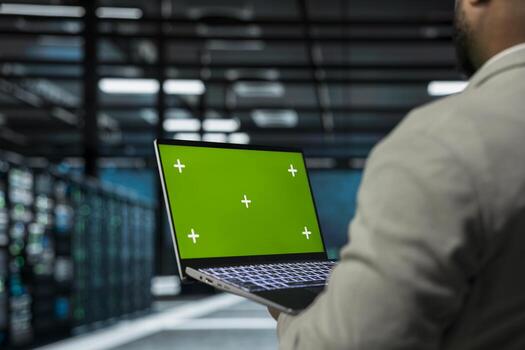Close up of system administrator in data center using green screen laptop to check for server performance issues. IT expert in server farm fixing errors slowing down hardware using mockup notebook photo