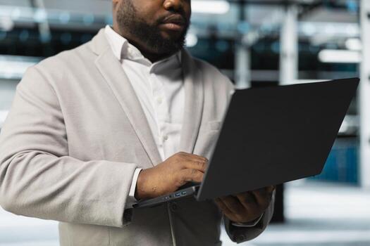 Close up of engineer in server hub checking recovery plan on laptop, monitoring hardware energy consumption. Data center IT expert using notebook, doing routine disk checks photo