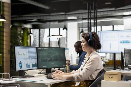 Office administrator uses focus music on headset to solve tasks, monitoring performance metrics at the workstation. Managing administrative tasks to ensure enterprise productivity and success. photo