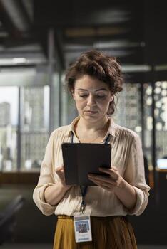 Administrator uses digital tools and analytics to improve corporate strategy, reviewing finance data insights on tablet to foster innovation and development in a modern office setting. photo