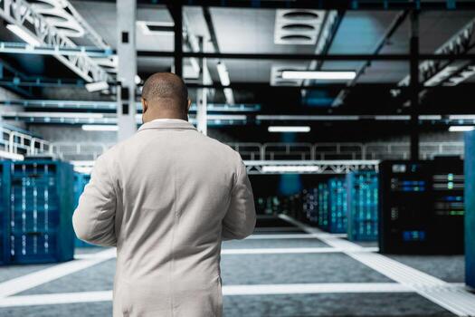 Admin walking in high tech data center, doing checkup to prolong equipment life span and increase uptime. African american server hub IT expert monitoring infrastructure mainframes, upgrading systems photo