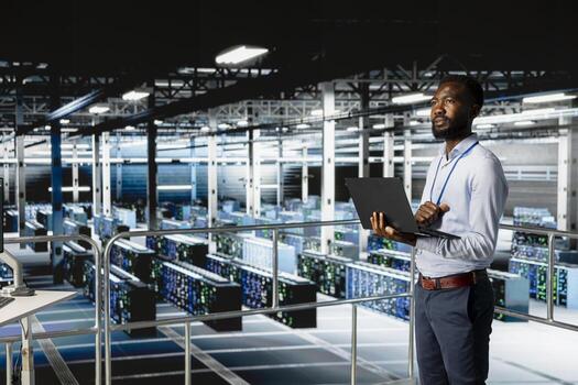 Black IT professional managing storage arrays for deep learning training workflows. Server hub engineer on industrial platform performing maintenance on servers handling AI processing tasks. photo