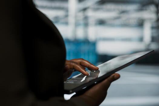Close up of engineer using tablet in data center to track metrics of gear used to host websites. Server room employee upgrading capacity of storage rackmounts running companies databases photo