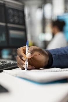 Close up of black business analyst takes notes on textbook in the office, examining charts and graphs to align company objectives with strategy. Drive progress and measurable performance. photo