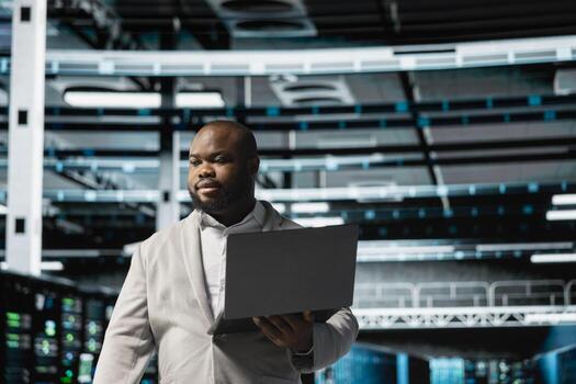 Data center admin using laptop to automate errors detection, troubleshooting backend operations. Server hub IT expert monitoring components for potential failures, conducting regular security audits photo