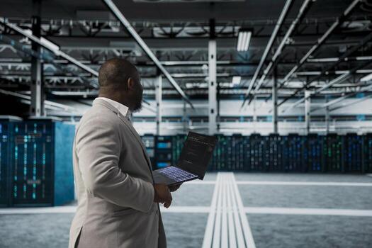Server room IT expert using programming scripts on laptop, doing debugging, monitoring error logs. Programmer in data center running lines of code on notebook, configuring rackmounts using application photo