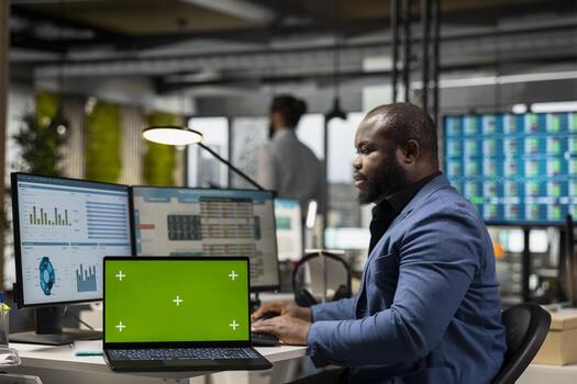 African american professional examines KPI data with chroma key screen, working on resource allocation forecast. Business management solutions to ensure productivity and success. photo