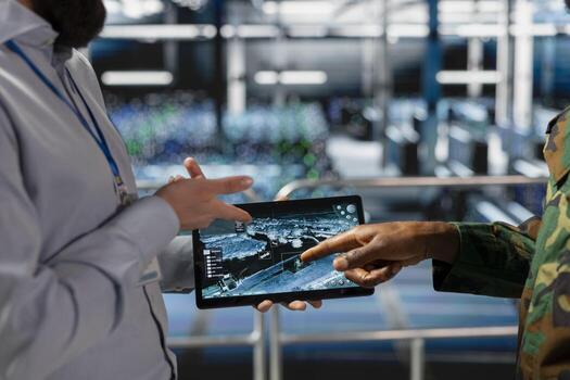 Military technician reviewing tactical dashboard on tablet screen in server hub, standing on industrial platform. Army expert using strategic communications and infrastructure software systems. photo