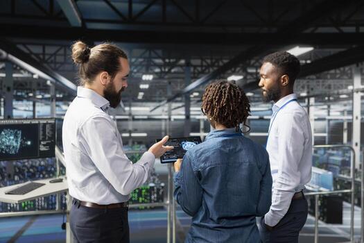 African american professionals handling performance metrics on tablet, ensuring technical workflow in server room. Employees team reviewing diagnostics for data center stability. photo