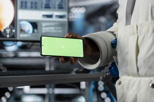 Scientists using mockup mobile phone in futuristic starship. Close up of researchers travelling in space conducting scientific experiments in orbit using green screen smartphone photo