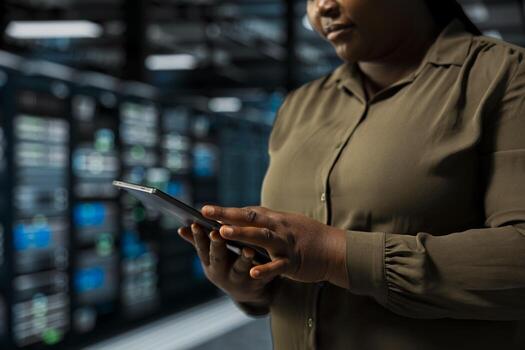 Close up of system administrator using tablet in data center to track metrics of gear used to host websites. Server room IT specialist upgrading capacity of storage rigs running companies databases photo