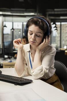 Young businesswoman focused on a podcast while she resolves office tasks, monitoring insights or KPI metrics on pc. Prepare strategy reports for expansion plans with digital tools, efficiency. photo