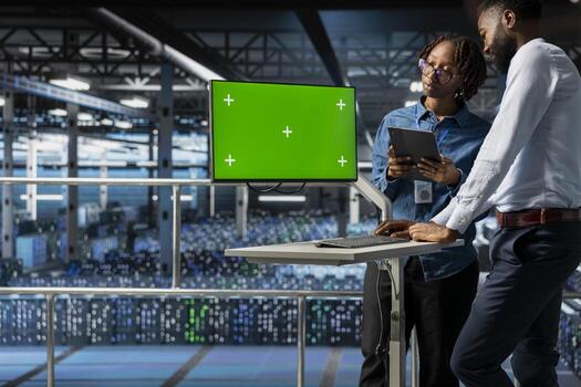African american engineer uses copy space on computer monitor in server hub, analyzing software systems data while he stands on industrial platform. Engineering AI tech configurations. photo