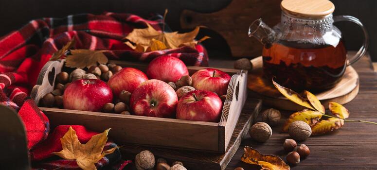 Red apples and nuts in a box, autumn leaves and a teapot with tea on the table web banner photo