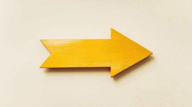 Yellow Wooden Arrow Points Right on a White Surface, Conveying Direction photo