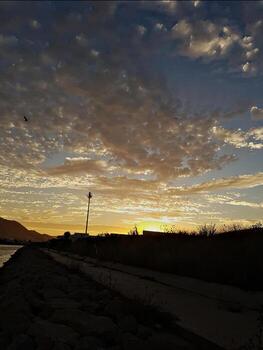 A golden sunset with a passway across a long valley with sky patterned clouds. the sun kisses the clouds, turning them into golden hues, while shadows in the foreground add depth to this scene photo