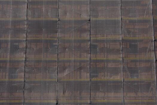 Building facade covered with semi-transparent construction mesh segmented vertically. Scaffolding and tension cables are visible through the mesh. photo