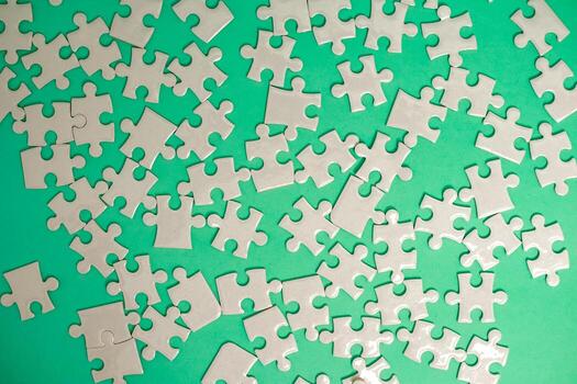 Scattered white puzzle pieces on a green background, representing connection and challenge, suitable for various design concepts photo