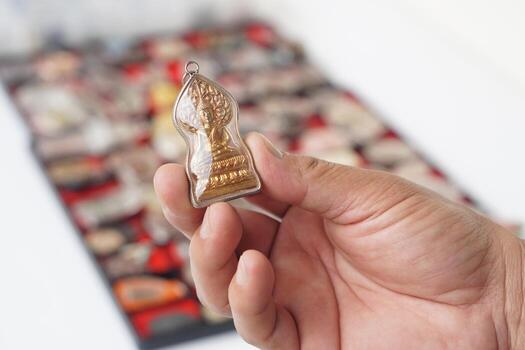 un mano participación un tailandés budista amuleto con un dorado Buda imagen encerrado en un claro cubrir, simbolizando fe y espiritual devoción. borroso antecedentes de amuleto colección agrega profundidad y contexto. foto