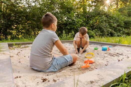 Two children are playing in a sandy area, creatively building and digging while enjoying the sun. The lush greenery around adds to the outdoor fun, creating a joyful atmosphere photo
