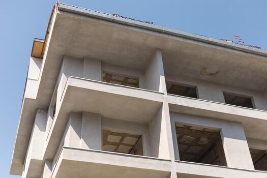 Ongoing construction work on a multi-story building with incomplete facades and open spaces under a bright blue sky. The structure showcases an urban development project photo