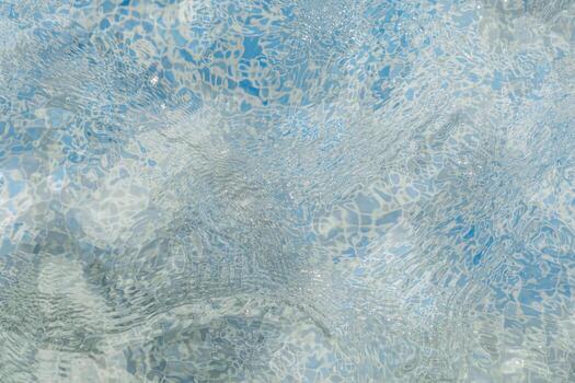 Clear water flows gently in a pool, reflecting sunlight and creating patterns on the surface. The tranquil blue tones evoke a sense of calm and relaxation photo