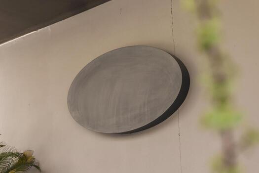 A large, circular artwork is displayed on a light-colored wall in a modern indoor setting. The design features minimalist styles and smooth surfaces, adding elegance to the space photo