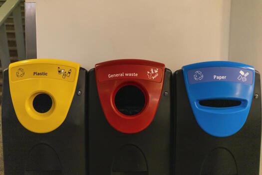 Three waste bins are arranged side by side in a hallway. Each bin is labeled distinctly for recycling plastic, general waste, and paper, promoting proper disposal practices photo
