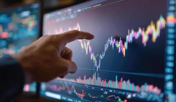 Close-up hand pointing at stock market chart on multiple computer screens photo