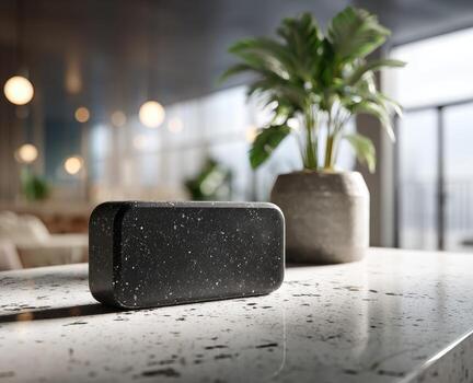 Dark gray speaker on a white speckled countertop with a plant in the background photo