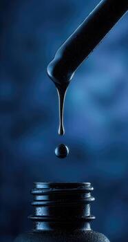 Black liquid drips from a pipette, poised over a dark bottle photo