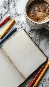 Open notebook with blank pages, coffee mug, and colored pens on marble surface photo