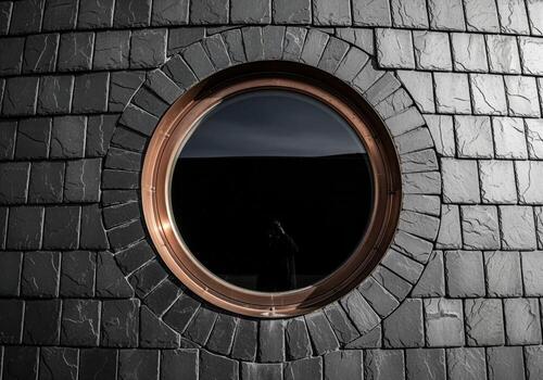 Circular porthole window with copper frame set in a dark slate tiled wall, modern architecture detail photo
