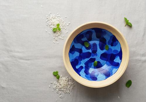 Flat lay of a decorative bamboo bowl with abstract blue pattern, scattered rice, and mint leaves photo